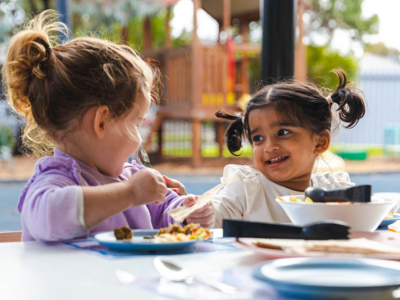 Two girls sitting at an outside table with plates of food in front of them at the Y's early learning centre